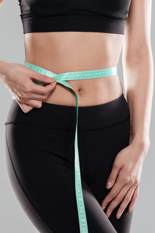 Woman Athlete Standing And Using Measuring Tape On Her Waist
